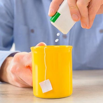 A man adds artificial sweetener tablets to a mug of tea